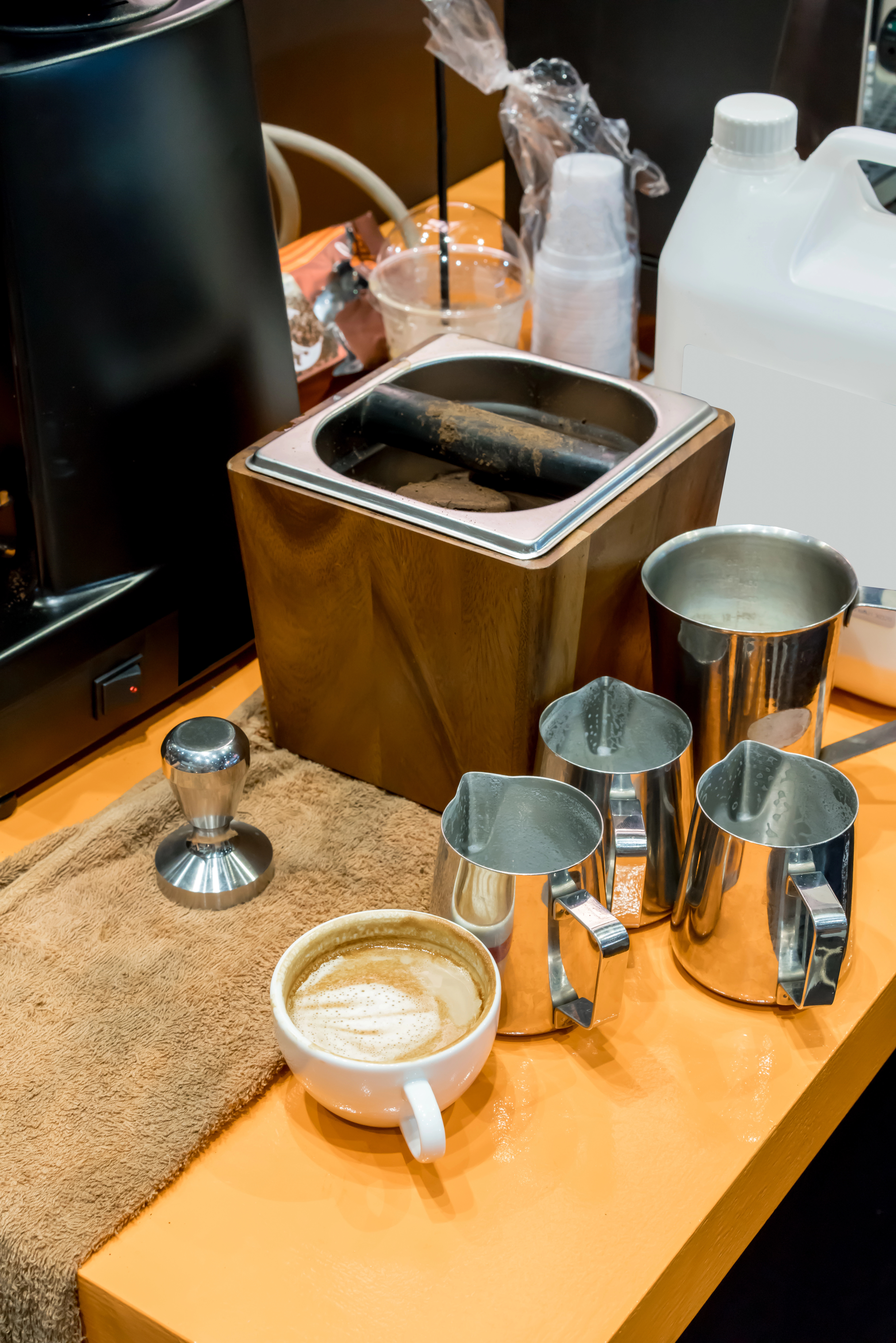 Variedad de insumos de cafetería ordenados en un mostrador, incluyendo granos de café, jarabes, jarras de leche y filtros, mostrando los elementos esenciales necesarios para un café | EdeComercial